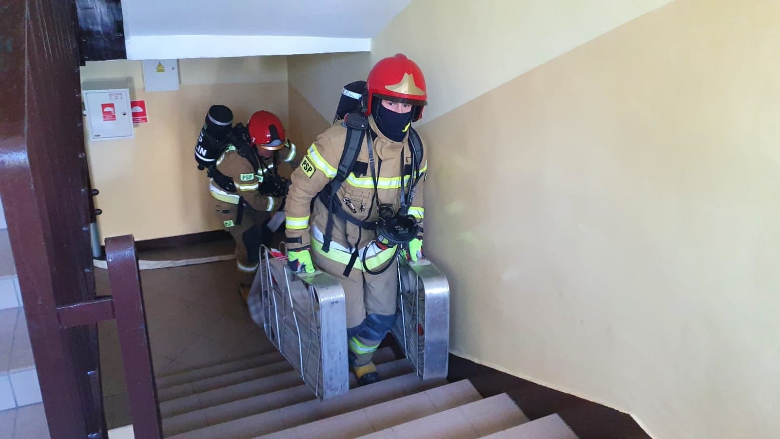 Strażacy wnoszący liny wężowe po klatce schodowej