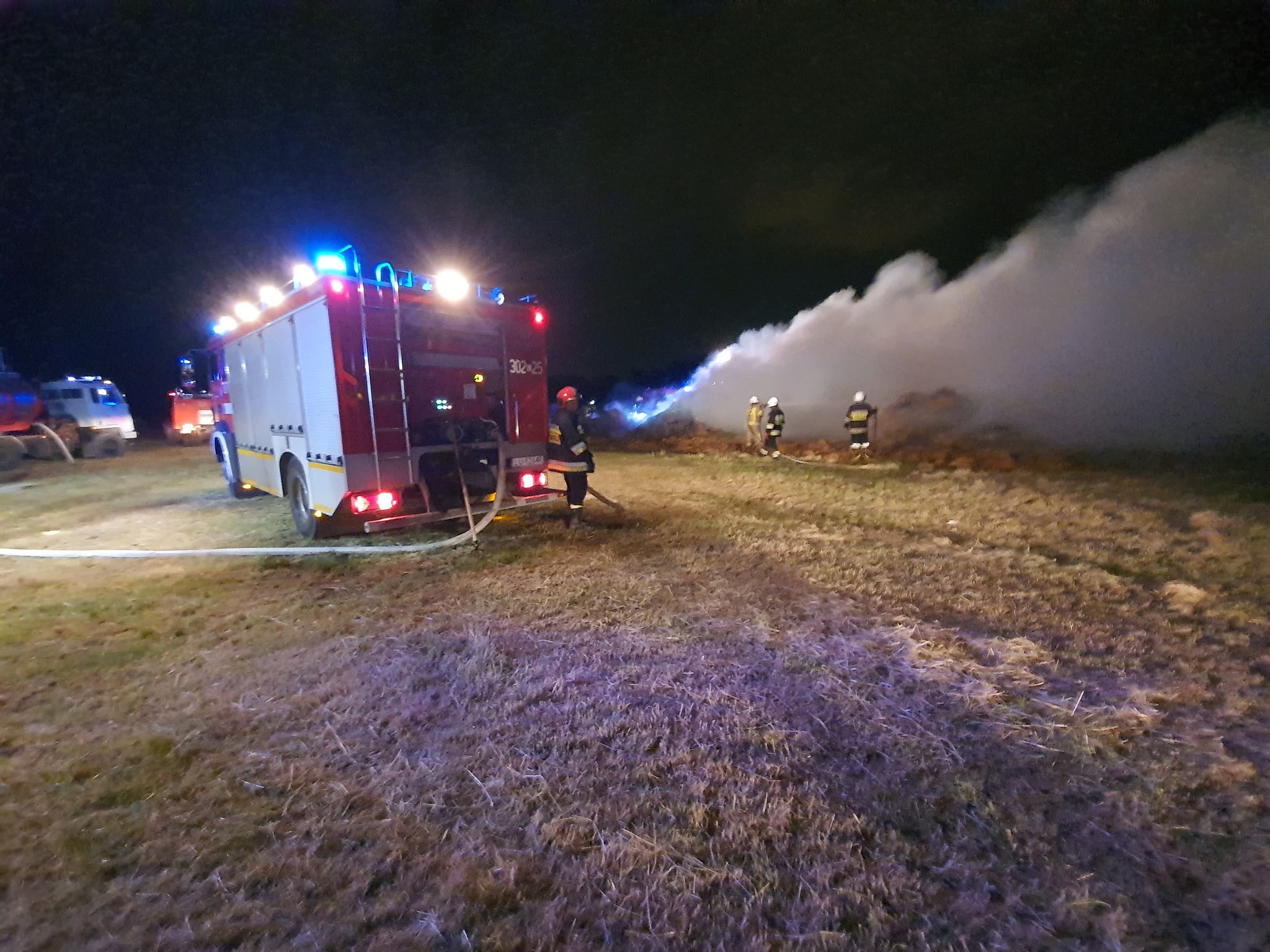 Samochód strażacki oraz kłęby dymu spowodowane pożarem słomy
