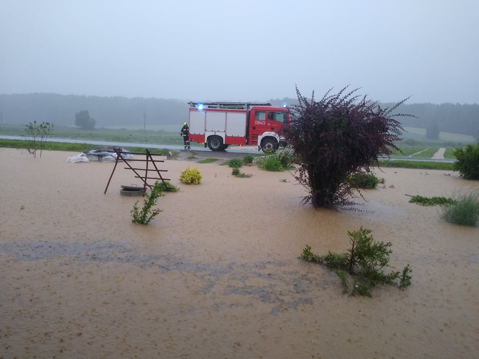 Samochód strażacki oraz strażak biorący udział w działaniach ratowniczych na terenach zalanych przez deszcz