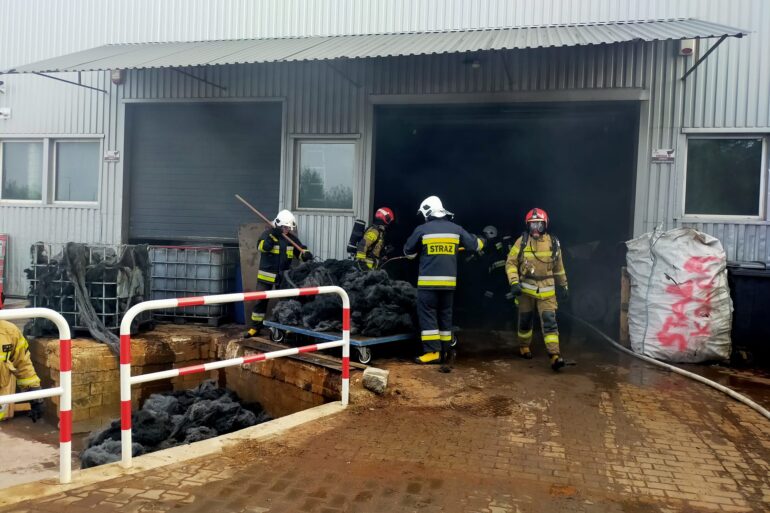 Strażacy gaszą palącą się wełnę stalową ubrani w aparaty ODO