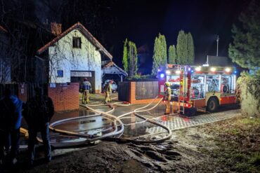 Dom objęty pożarem, pojazd pożarniczy oraz strażacy